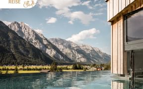 Infinity pool at Charme-Hotel Kristall in Leutasch with dramatic Alpine mountain backdrop and cloudy blue sky.