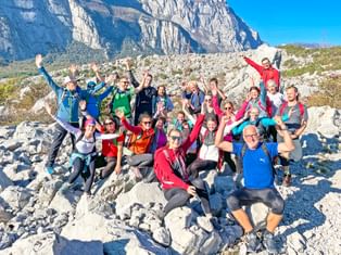 Gruppe aus Wanderern hebt die Hände in die Höhe, Berge im Hintergrund, Sonnenschein