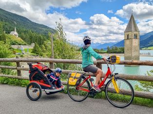 Frau auf Fahrrad mit Kinderanhänger am Reschensee
