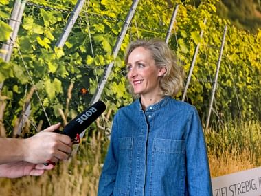 Blonde woman speaks into a microphone and smiles