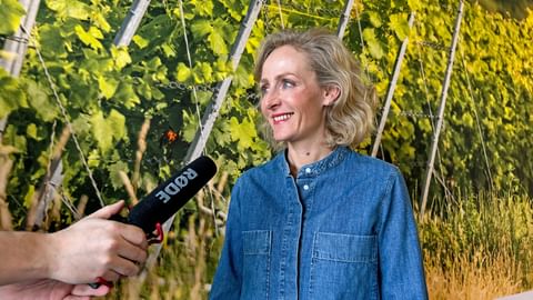 Blonde Frau spricht in ein Mikrofon und lächelt dabei