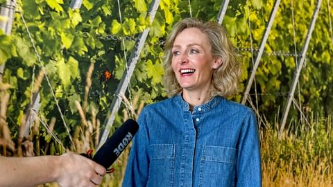 Blonde woman in a denim shirt laughs and speaks into a microphone